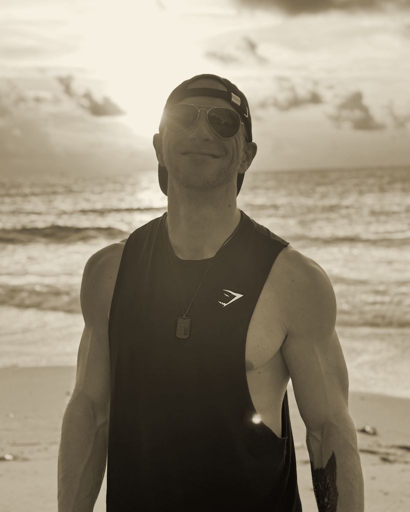 Max am Strand im Gegenlicht, mit Cap und Sonnenbrille, lächelnd.