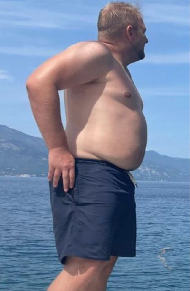 Max vorher mit 120 Kilo, ohne Shirt auf einem Boot, im Hintergrund Meer und Berge.